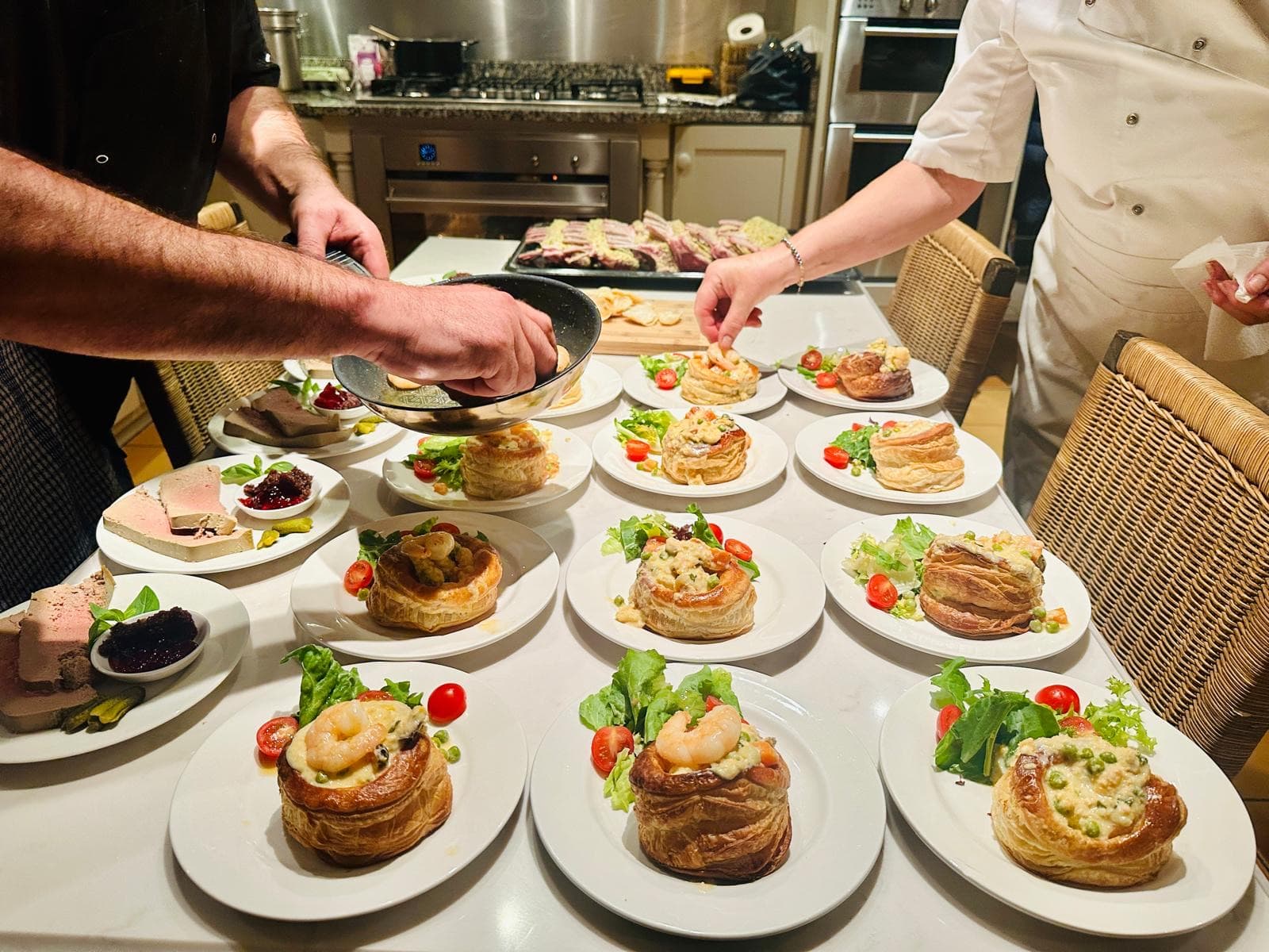 A buffet mid-service — plates of prawn vol-au-vents on dressed salad and slices of pâté with chutney laid out across a marble island, chefs working behind.